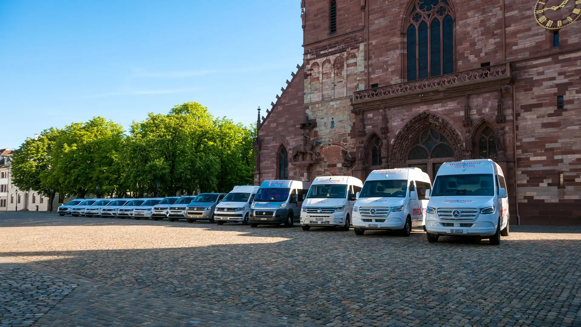 Die ganze Fahrzeugflotte von Mobimed Patiententransport in einer Reihe vor dem Basler Münster